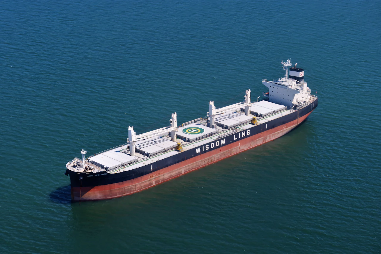 A laden bulk carrier rests on calm open water